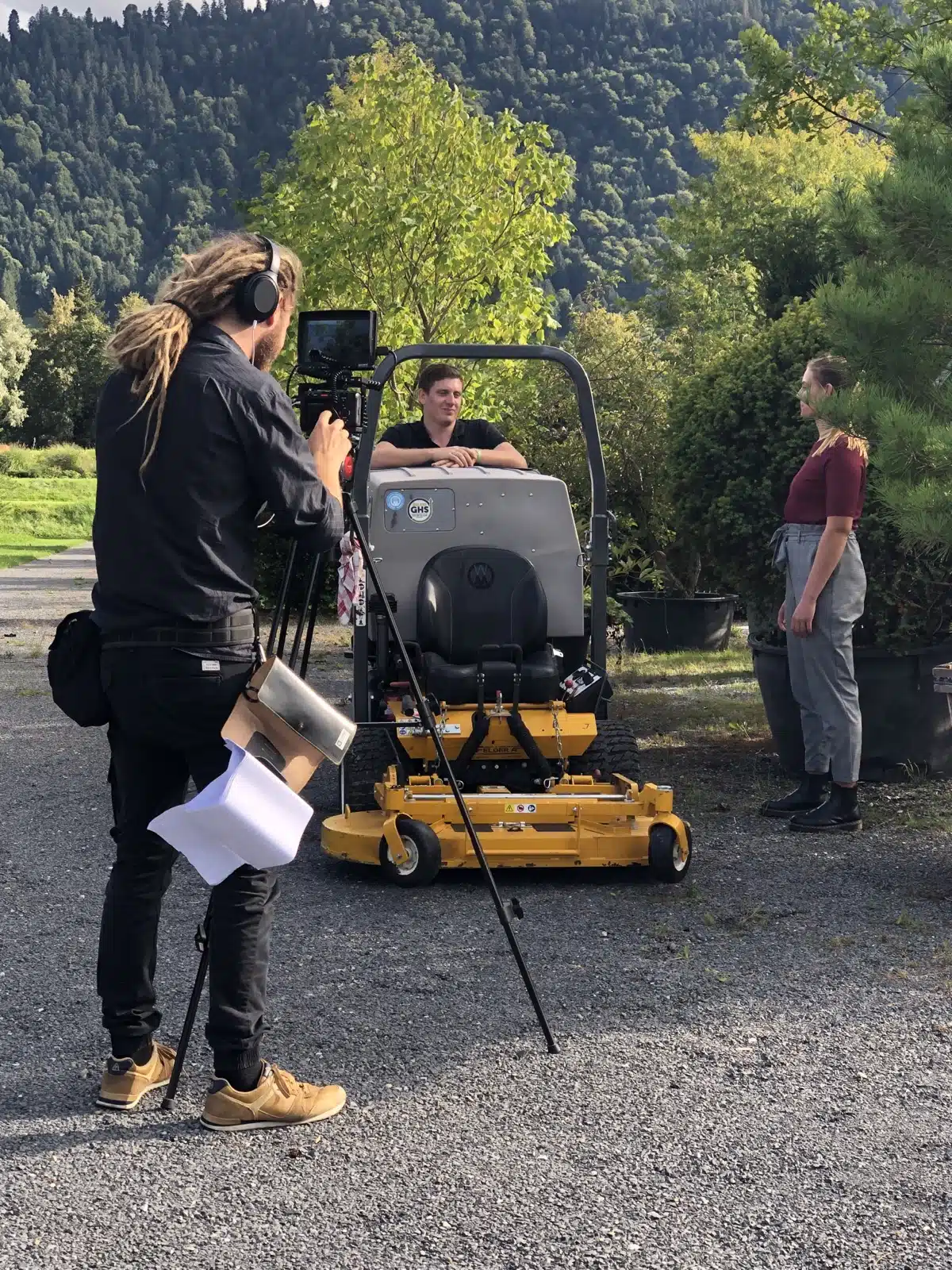 Filmteam be der Arbeit mit schaupielerin in einem Gartenbaubetrieb in der schweiz switzerland in der nähe von basel mit einem grossen Rasenmäher auf dem Bild.